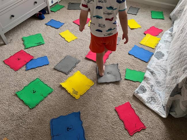 image of reviewer's kid standing on a gray game tile surrounded by other colored tiles on the floor