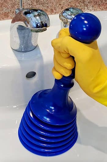 Model using a small blue plunger on a sink 