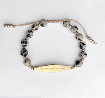 Black and white beaded bracelet with size adjusting strings and a gold charm that reads 