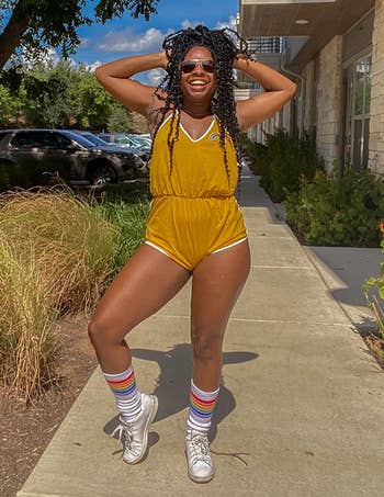 Person posing outdoors successful a stylish romper and sneakers, wearing sunglasses and socks with stripes, lasting connected a paved sidewalk beside writer and trees