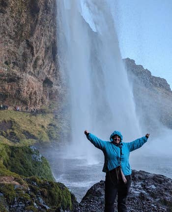 person wearing blue winter jacket in front of Icelandic waterfall