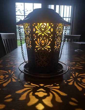 The lantern lit up casting patterns from the cutouts in it over a table 