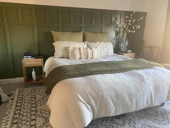 Stylish chamber  with a achromatic  and greenish  bed, patterned rug, bedside tables, and decorative plants, highlighting cozy location  decor