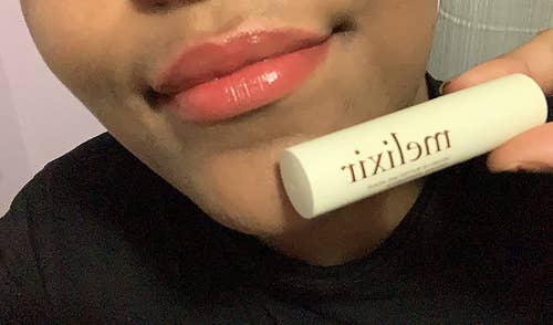 a reviewer wearing the lip butter and holding up a tube of it 