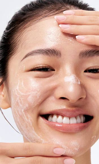 Person smiling, applying facial cleanser successful a skincare routine. Close-up of a fresh, cleanable look with soap lather, highlighting skincare techniques