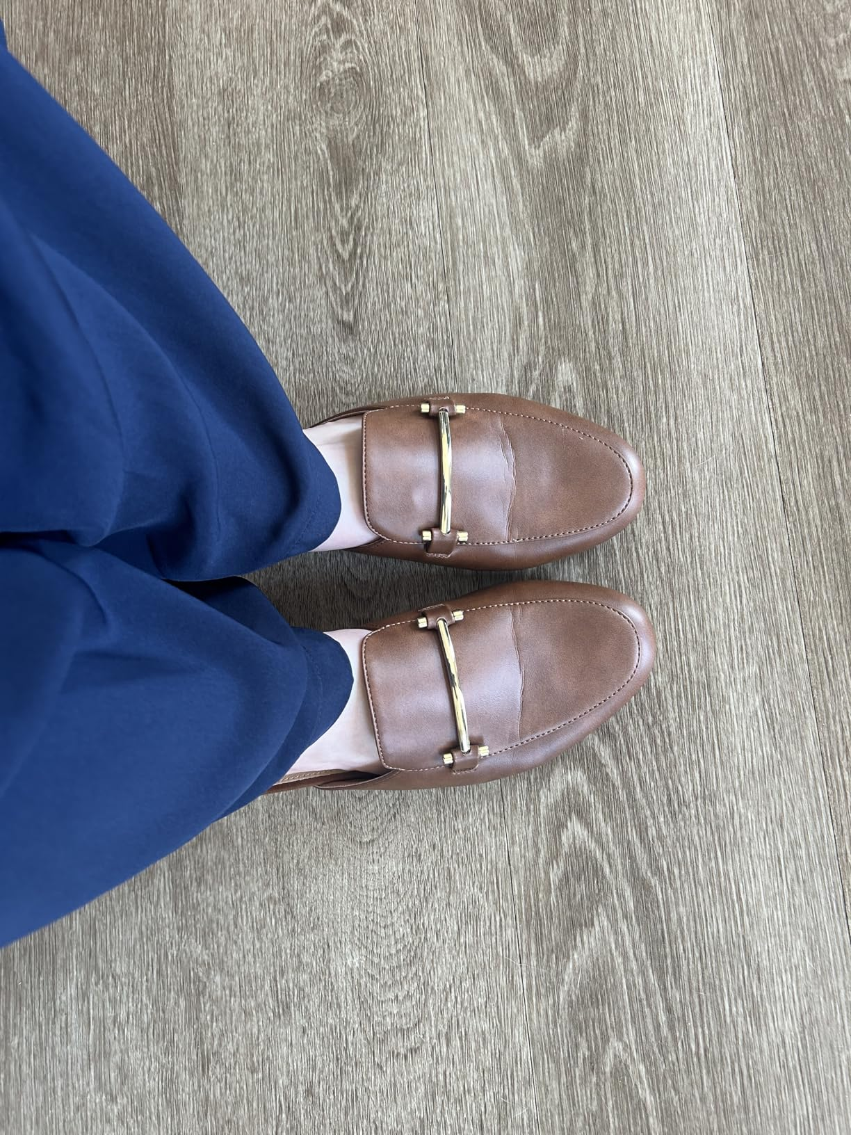 Person wearing brownish  loafers with golden  barroom  item  and acheronian  pants stands connected  woody  floor