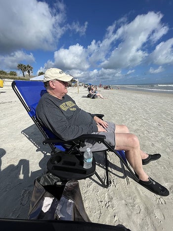 reviewer photo of them lounging in the blue recliner on a beach