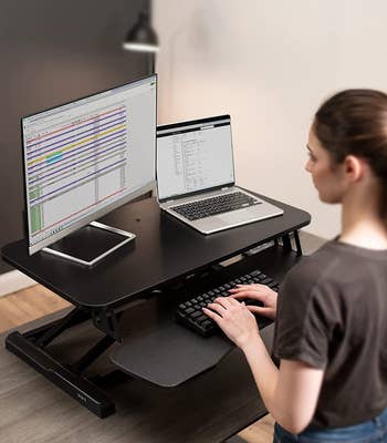 Model using sit-to-stand desk converter in with laptop and monitor on it