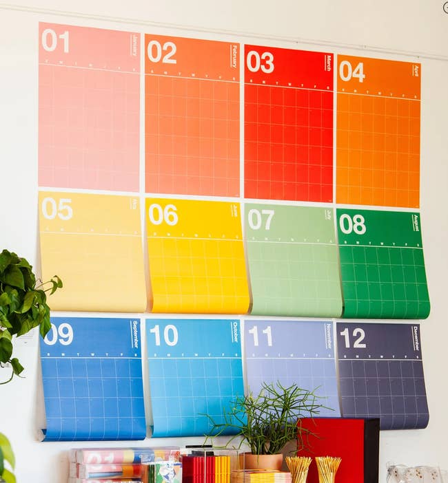 a 12 month undated calendar with each month hanging in a separate page on the wall in a different color of the rainbow 