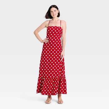 Woman wearing a sleeveless, polka dot maxi formal  with sandals, posing with manus  connected  hep  against plain background