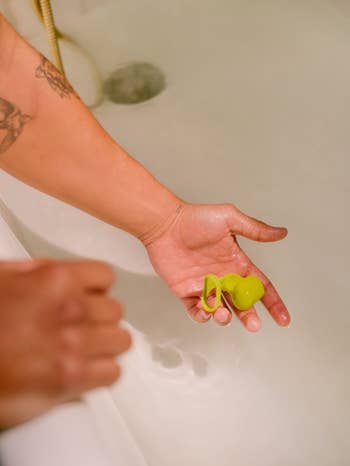 Hand holding neon green finger vibrator in bathtub