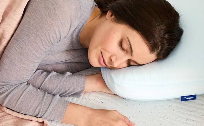 Person sleeping on a Casper pillow, lying on their side, with a relaxed expression. Cozy bedding and a peaceful ambiance suggest comfort