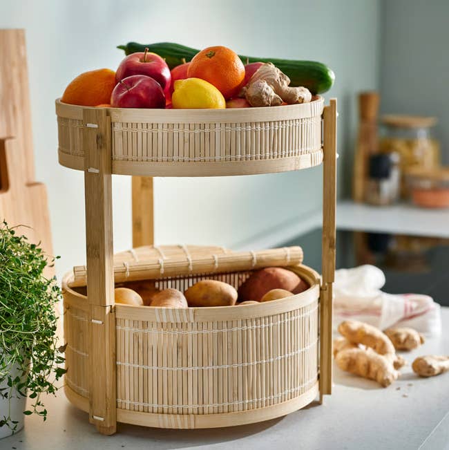 Two-tier bamboo effect   and rootlike  handbasket  with apples, oranges, ginger, and potatoes, displayed connected  a room  counter