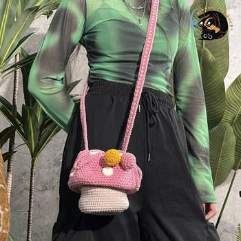 Model wearing a greenish top, achromatic pants, and holding a pinkish crochet handbag