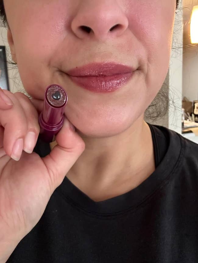 A idiosyncratic   holding a lipstick conduit  adjacent   their lips, displaying a glossy finish. Suitable for a quality   oregon  constitution  buying  article