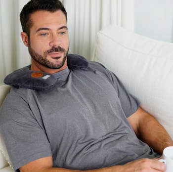 Man relaxing connected a sofa wearing a cervix massager, holding a mug, and gazing forward
