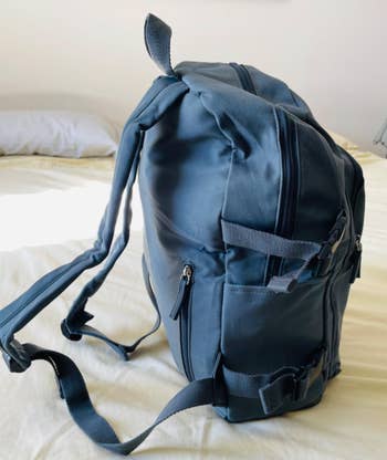 Sleek, modern backpack with multiple zippers and adjustable straps on a bed, ideal for shopping and travel