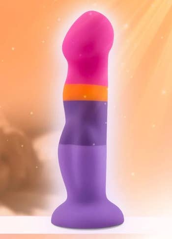 A multicolored silicone dildo stands upright against a soft, blurred background