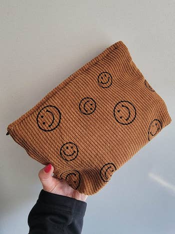 a reviewers brown corduroy makeup bag with black smiley faces on it