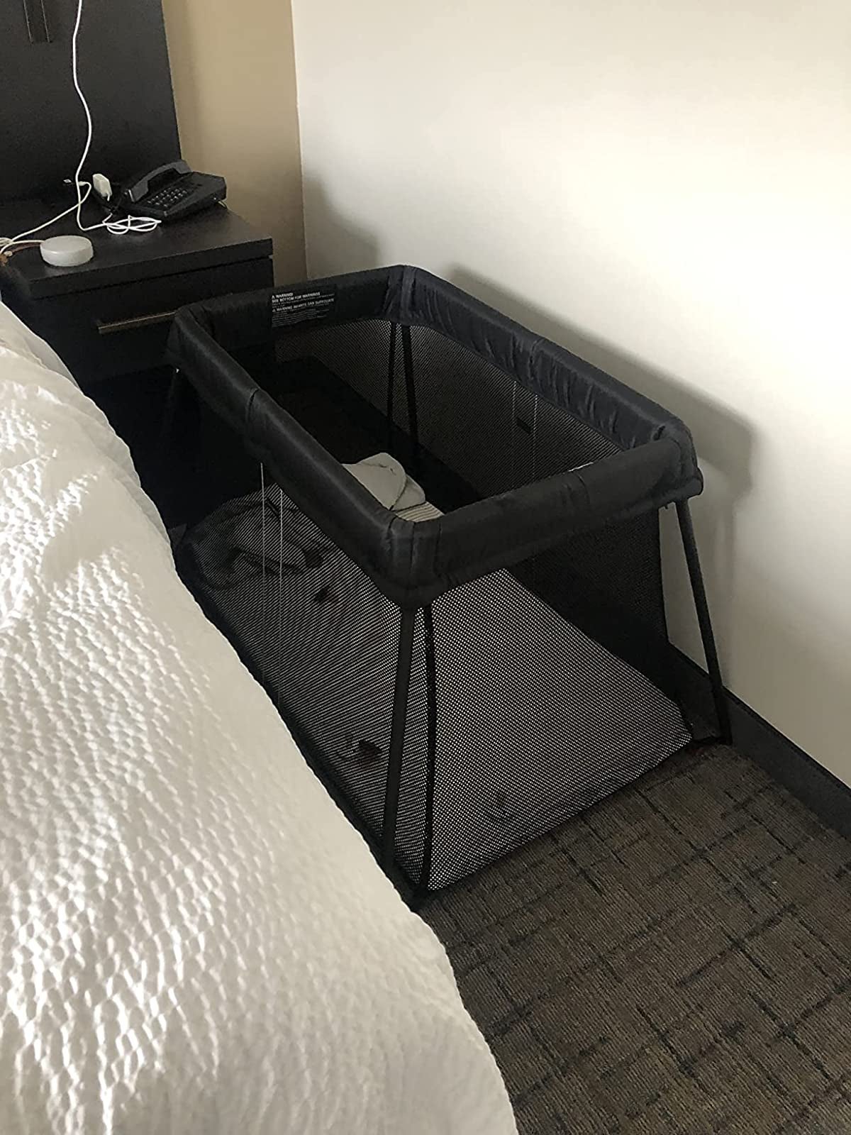 hotel customer picture of the travel baby crib in between a hotel bed and wall