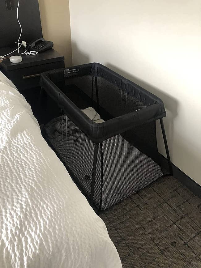 reviewer image of the travel crib in between a hotel bed and wall