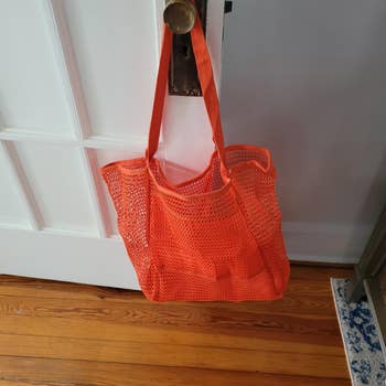 Orange mesh tote bag hanging on a door knob, suitable for shopping or carrying groceries