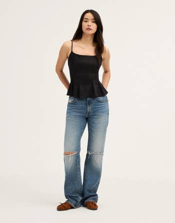 A person wearing a stylish black peplum camisole and ripped blue jeans poses for a fashion photo