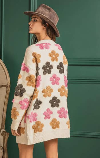 a model in a long tan cardigan with plush flowers on it showing the back