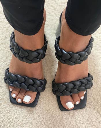 A pair of feet wearing black braided strap sandals