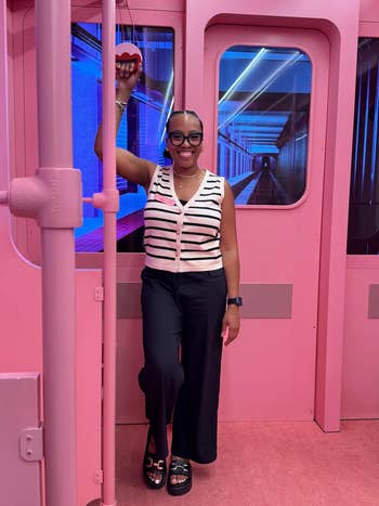Person successful  a striped apical  and achromatic  pants poses successful  a pink-themed setting, holding a heart-shaped decoration