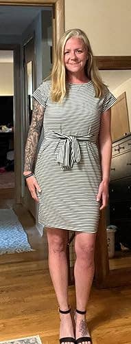 Person successful  a striped formal  with a tie-front item  stands successful  a room, smiling, and wearing sandals. They person  a tattoo connected  1  arm