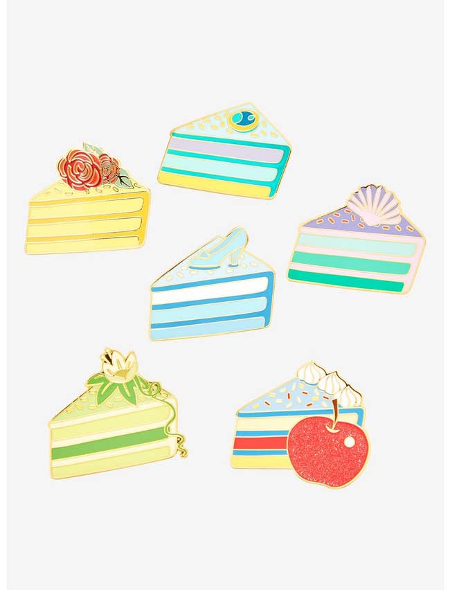 small cake slice shaped pins with designs inspired by belle cinderella, snow white, tiana, ariel, and jasmine