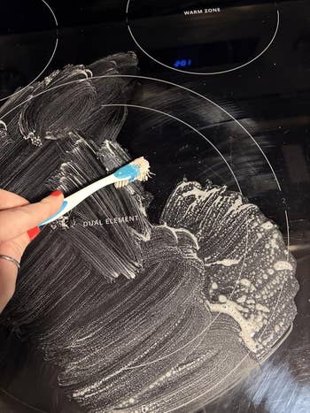 A idiosyncratic   scrubs a solid  stovetop with a toothbrush and cleaning paste, showcasing a cleaning method  for household   chores