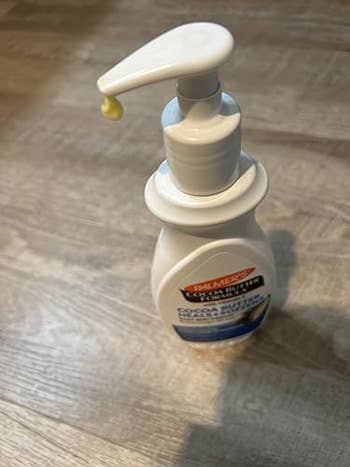 Pump vessel of Palmer's Cocoa Butter Daily Skin Therapy Lotion connected a woody surface