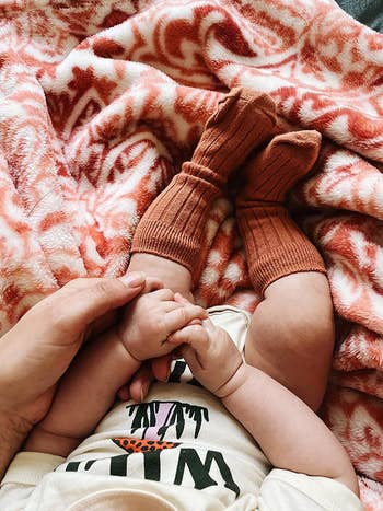 a reviewer photo of their baby wearing the socks with a onesie