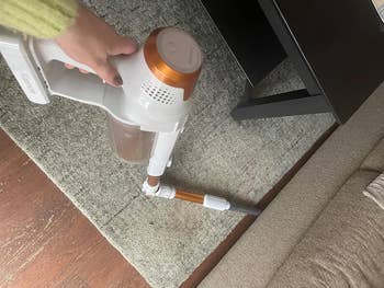 a reviewer holding a handheld vacuum cleaner, vacuuming a carpet near a table