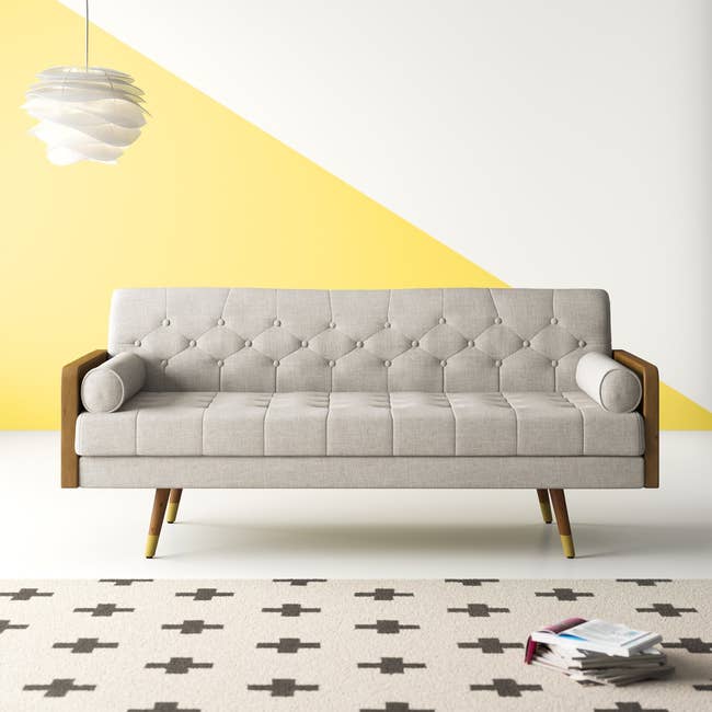 tufted mid century modern sofa with angled legs, two oval pillows, and wood sides 