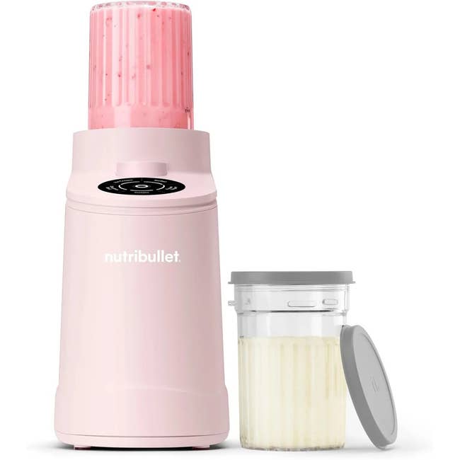 A NutriBullet blender in pink with a pink smoothie in the cup and an additional small cup with lid, designed for convenient, healthy blending