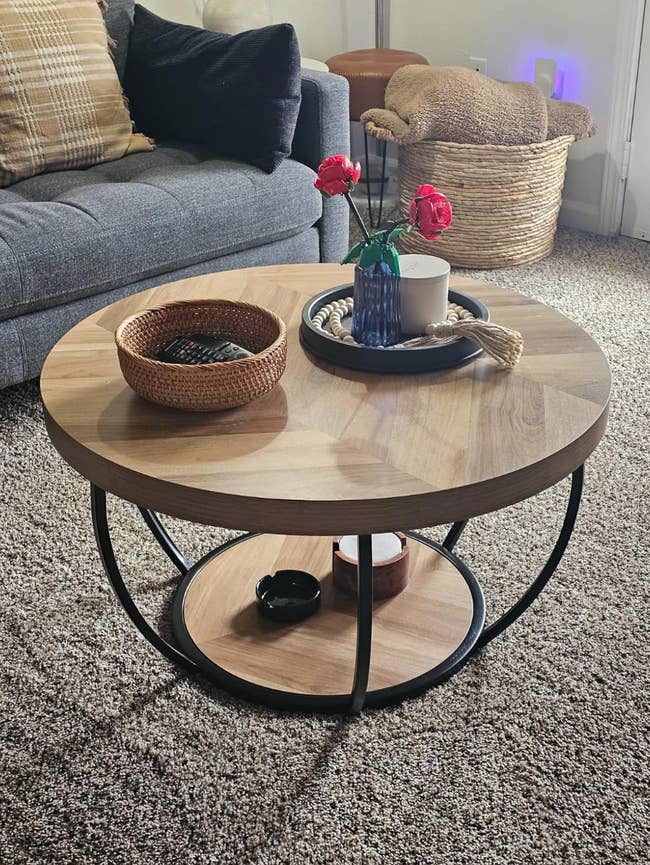 Modern wooden coffee table with black metal legs, adorned with a vase of red roses, a candle, and a woven basket on a carpeted floor
