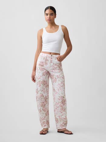 Person wearing a achromatic vessel top, floral-patterned pants, and flip-flops. Fashion posed against a plain backdrop, suitable for buying content