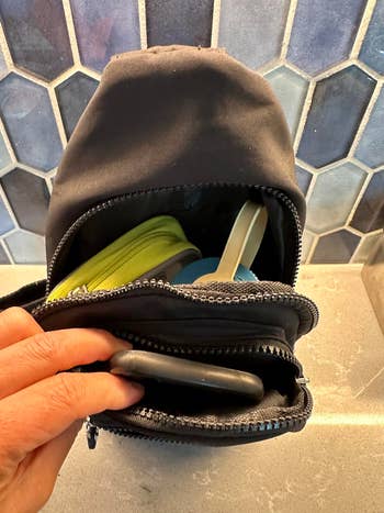 Small backpack opened to show items like a yellow pouch and a smartphone inside, placed against a tiled background