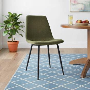 Modern eating  seat  with a sleek plan  connected  a bluish  patterned rug, beside a array  with apples and a drink, and a works  successful  the background