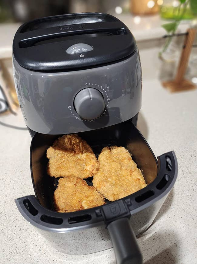 gray air fryer with basin opened to show crispy chicken 