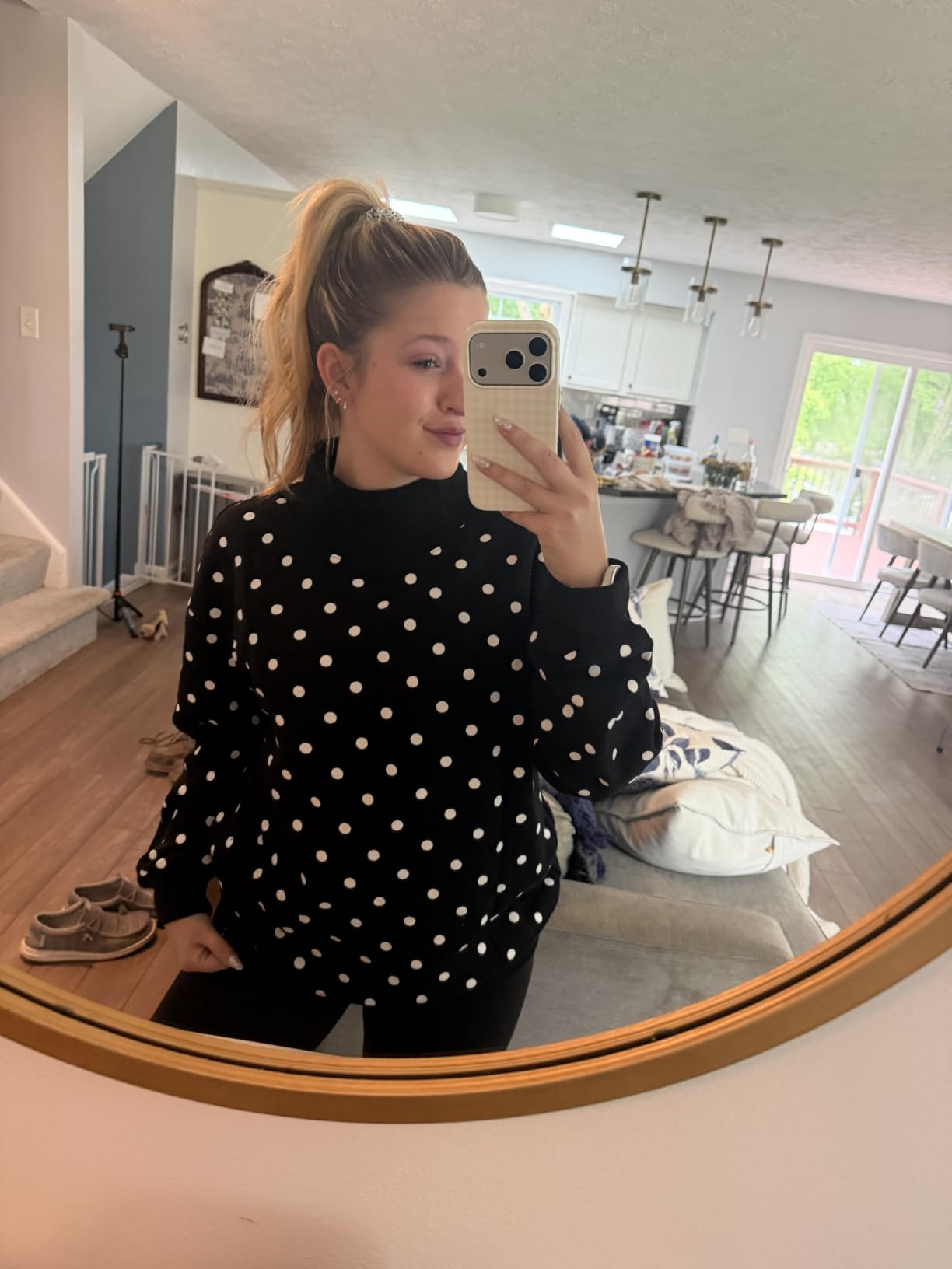 Person taking a reflector  selfie successful  a modern   surviving  room, wearing a polka dot sweater and achromatic  pants, with hairsbreadth  successful  a ponytail