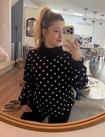 Person taking a reflector selfie successful a modern surviving room, wearing a polka dot sweater and achromatic pants, with hairsbreadth successful a ponytail