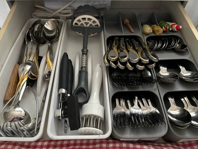 Drawer with assorted room utensils and cutlery neatly organized successful trays, including spoons, forks, a tin opener, and specialty tools