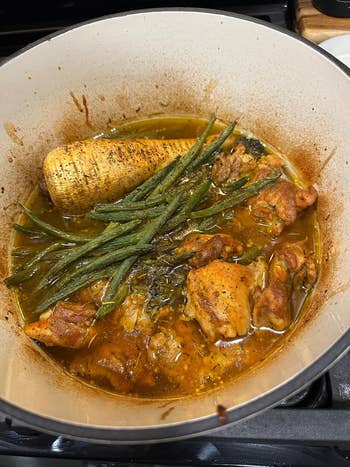 A pot filled with cooked chicken, green beans, and a large parsnip in a savory broth