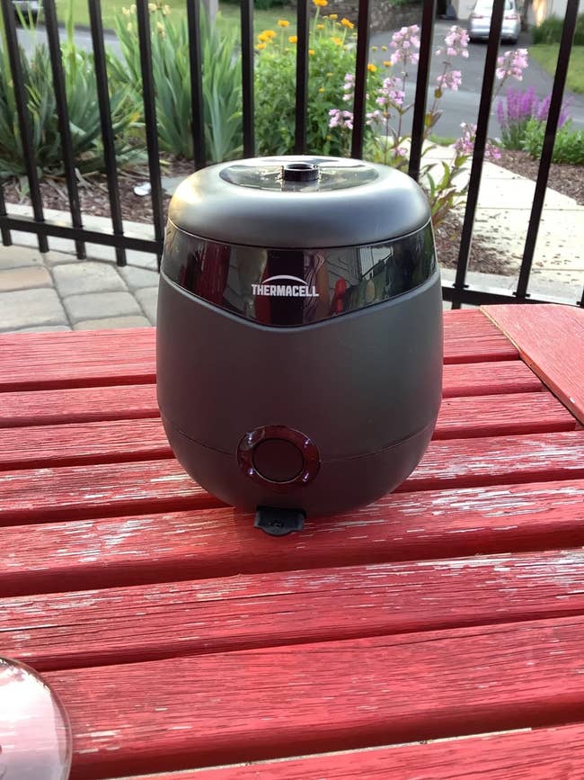 Thermacell device on a red patio table outdoors, designed for mosquito repellent use in gardens or patios