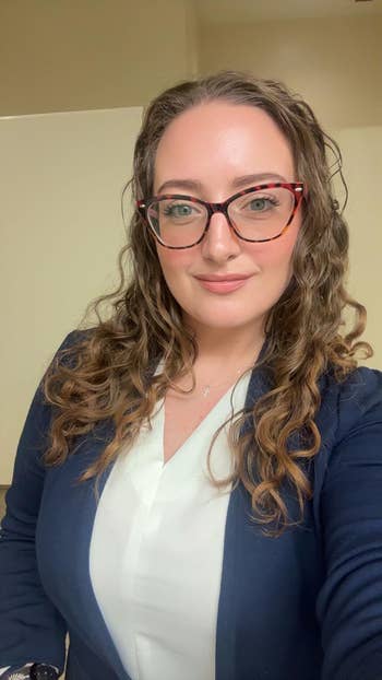 Person wearing glasses and a blazer, smiling indoors