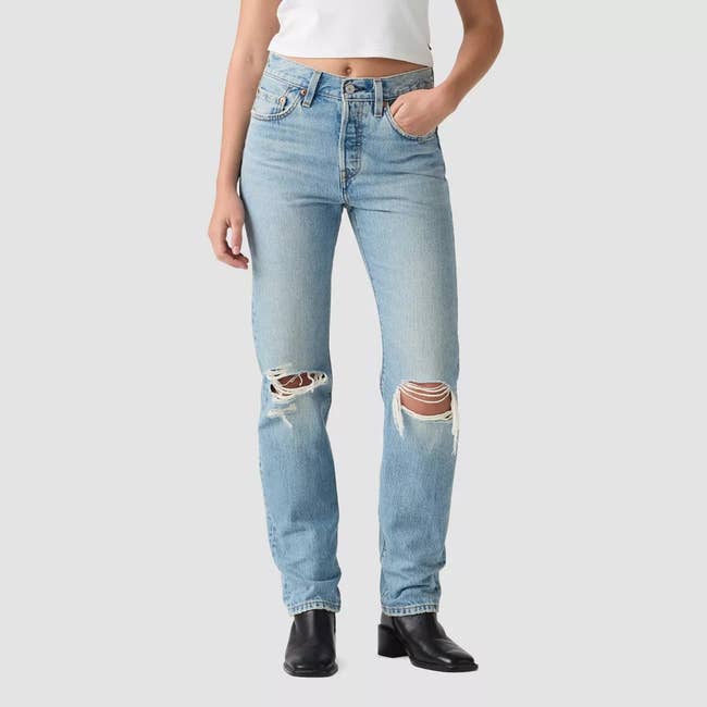 Person wearing high-waisted ripped jeans and a achromatic harvest top, lasting with 1 manus successful pocket, paired with achromatic ankle boots